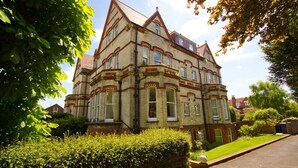 A large, multi-story house with a prominent corner turret, surrounded by well-maintained hedges and a clear driveway. - Great location - sleeps up to five guests, just moments from the beach and town (Eastbourne)