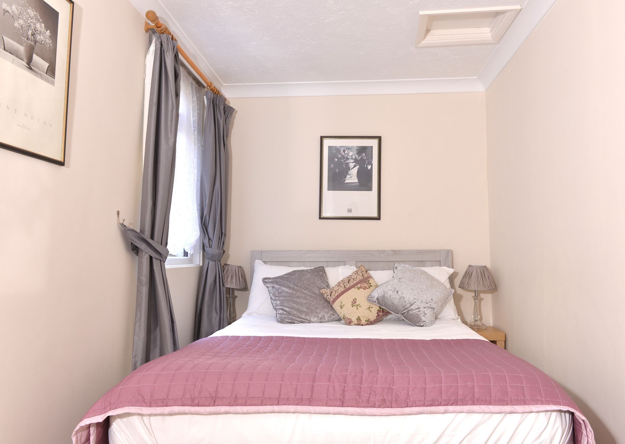 Une chambre à coucher avec un lit, une fenêtre avec des rideaux, un tableau encadré au mur et une lampe de chevet.