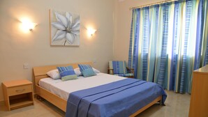 A bedroom with a bed, bedside tables, a chair, a wall-mounted lamp, and a window with curtains. - Summer Haven, with breathtaking views and Private Swimming Pool (Mellieha)