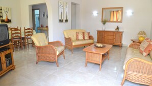 A living room with wicker furniture, a television, and a dining area with chairs and a table. - Summer Haven, with breathtaking views and Private Swimming Pool (Mellieha)