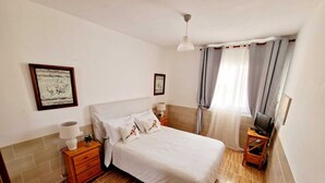 A bedroom with a bed, bedside tables, a lamp, a TV on a stand, and curtains. - IDEAL WITH CHILDREN, WIFI, WHITE SAND BEACH. (Costa Calma, Pajara)