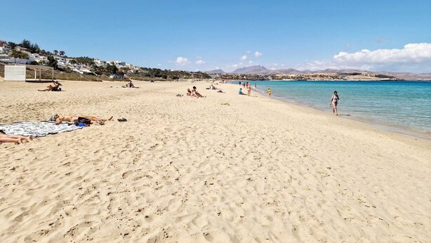 A wide sandy beach with clear blue water, people sunbathing and swimming, and a hilly landscape in the background. - IDEAL WITH CHILDREN, WIFI, WHITE SAND BEACH. (Costa Calma, Pajara)
