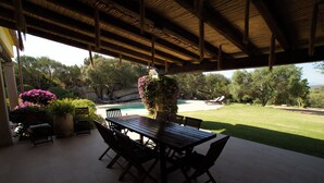 An outdoor patio with a wooden table and chairs, surrounded by greenery and a view of a swimming pool. - Villa set in the beautiful countryside, 5 mins to fantastic beaches & Islands (Arzachena)