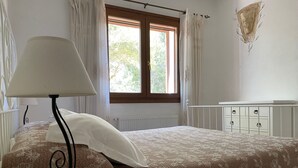 A bedroom with a bed, a nightstand, a lamp, a window with curtains, and a radiator. - Villa set in the beautiful countryside, 5 mins to fantastic beaches & Islands (Arzachena)