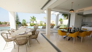 Un espace repas moderne avec vue sur la piscine, des sièges d’extérieur et une cuisine en arrière-plan.