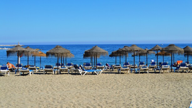 Une plage bordée de rangées de chaises longues et d’ombrelles en chaume.