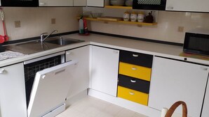 Cozinha moderna com armários brancos, lava-louças, pia e micro-ondas. Há gavetas amarelas e uma cesta de vime com limões no balcão.