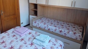 Quarto com duas camas de solteiro, um guarda-roupa de madeira e uma porta.