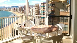 A balcony with a table and chairs, overlooking a beach and cityscape. - Levante beachfront vacation with spectacular views and sunny terrace (Benidorm)