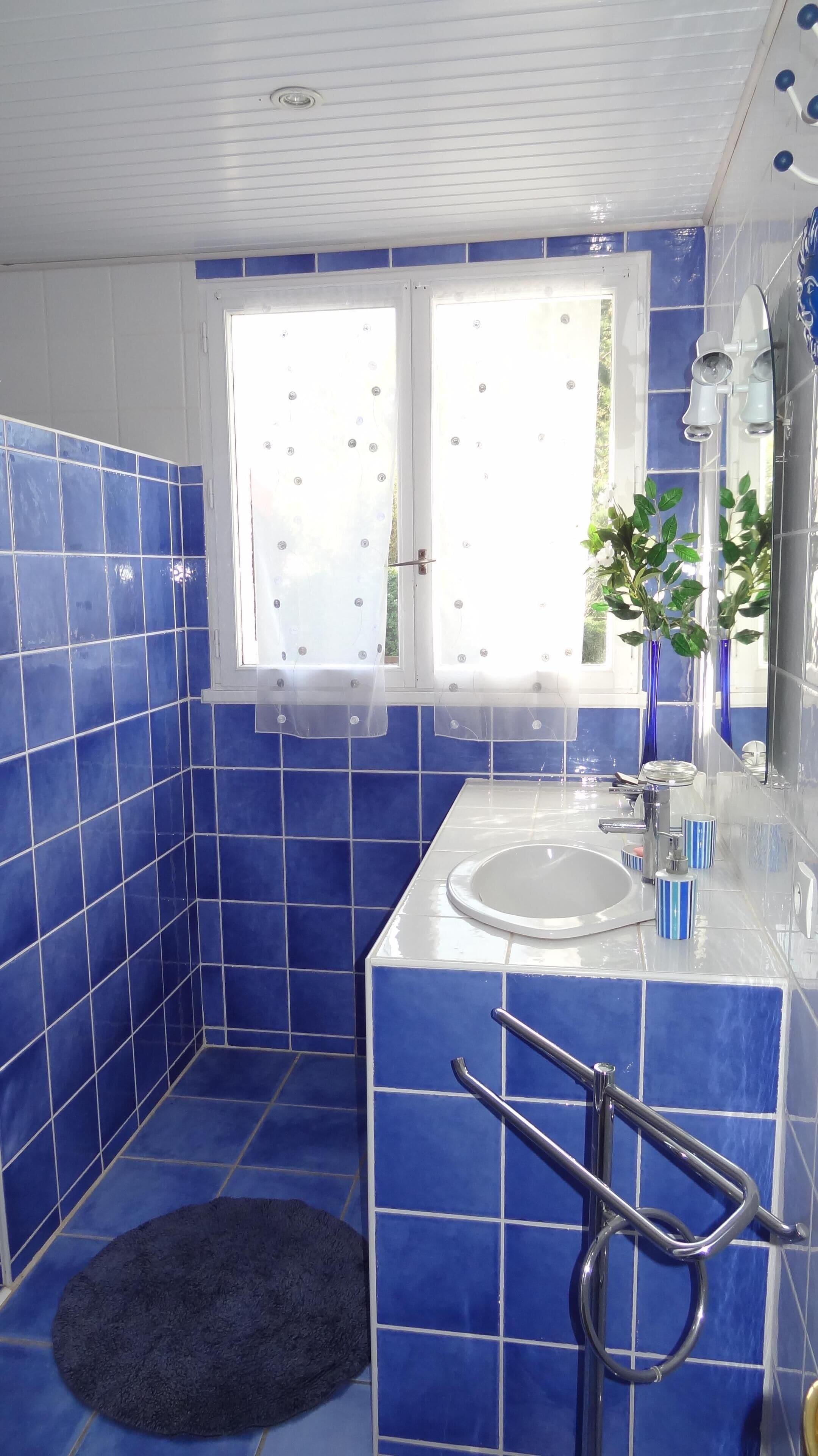 A bathroom with blue tiles, a white sink, a mirror, and a window with curtains.