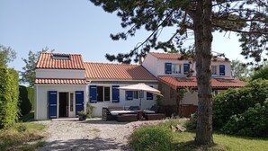 Ein zweigeschossiges Haus mit einem Ziegeldach, einer Terrasse mit Tisch und Stühlen und einem Schotterweg.