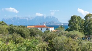Un bâtiment blanc avec un toit rouge, entouré de verdure et offrant une vue sur une zone côtière avec des montagnes en arrière-plan.
