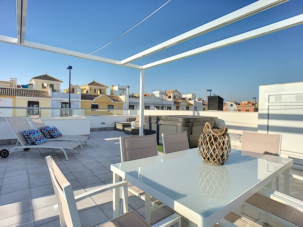 Une terrasse sur le toit avec une table en verre, des chaises et un vase décoratif.