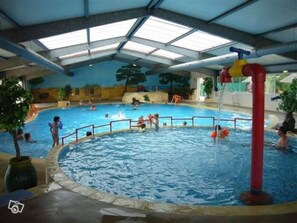 Piscina interior com várias pistas de natação, um tobogã central e uma estrutura coberta com claraboias.