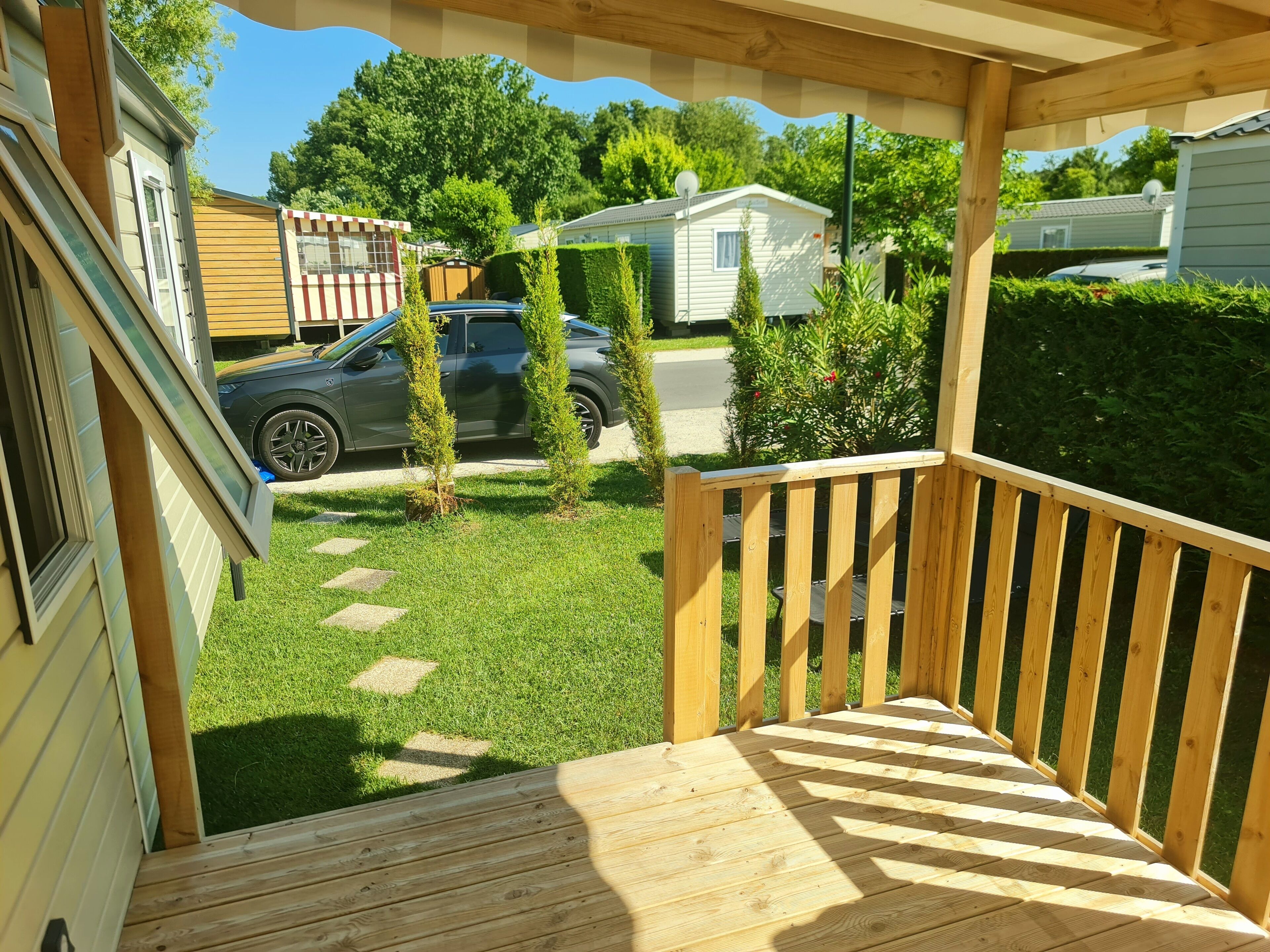 Eine Holzterrasse mit Geländer, einer Rasenfläche und einem geparkten Auto im Hintergrund.