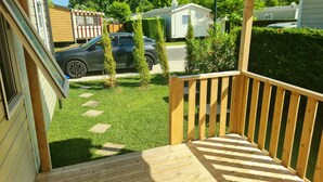 A wooden deck with a railing, a lawn, and a parked car in the background. - **** SPACIOUS MOBILE HOME 1/8 PERS LES CHARMETTES **** (Les Mathes)