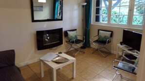 A living room with a TV, two chairs, a small table, a window with curtains, and a ceiling light. - Pretty detached house. not overlooked, swimming pool. near Sarlat/Rocamadour (lachapelle haute)