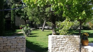 Eine Steinsicht, eine gepflasterte Terrasse und ein Garten mit Bäumen und Rasen.