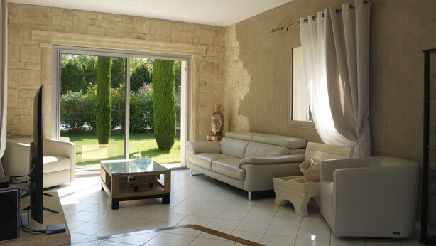 Ein geräumiges Wohnzimmer mit Steinswand, einem großen Schiebeglasfenster zum Garten, einem beigen Sofa, einem Couchtisch und einem Fernseher.