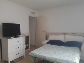 Une chambre à coucher avec un lit, un téléviseur posé sur une commode et une porte donnant sur une autre pièce.