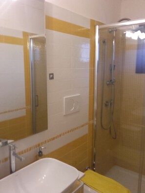Une salle de bain avec un lavabo blanc, des murs recouverts de carreaux jaunes, une douche en verre et un miroir.