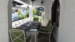 Un comedor con una mesa larga dispuesta para una comida, sillas y un aro de baloncesto al fondo.