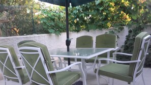 Une terrasse avec une table en verre et des chaises en métal blanc dotées de coussins verts.