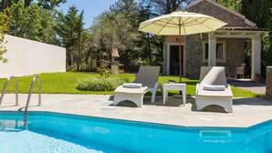 Una piscina con dos sillas de descanso y una pérgola con sombrilla.