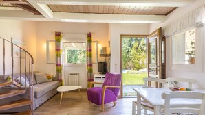 Una sala de estar acogedora con un sofá, un sillón púrpura, una mesa blanca y una escalera.