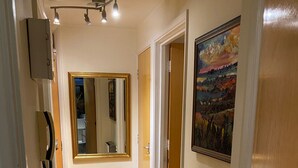 A hallway with wooden flooring, a mirror, a painting, and a fire extinguisher. - Modern London Tower Bridge apartment (London)