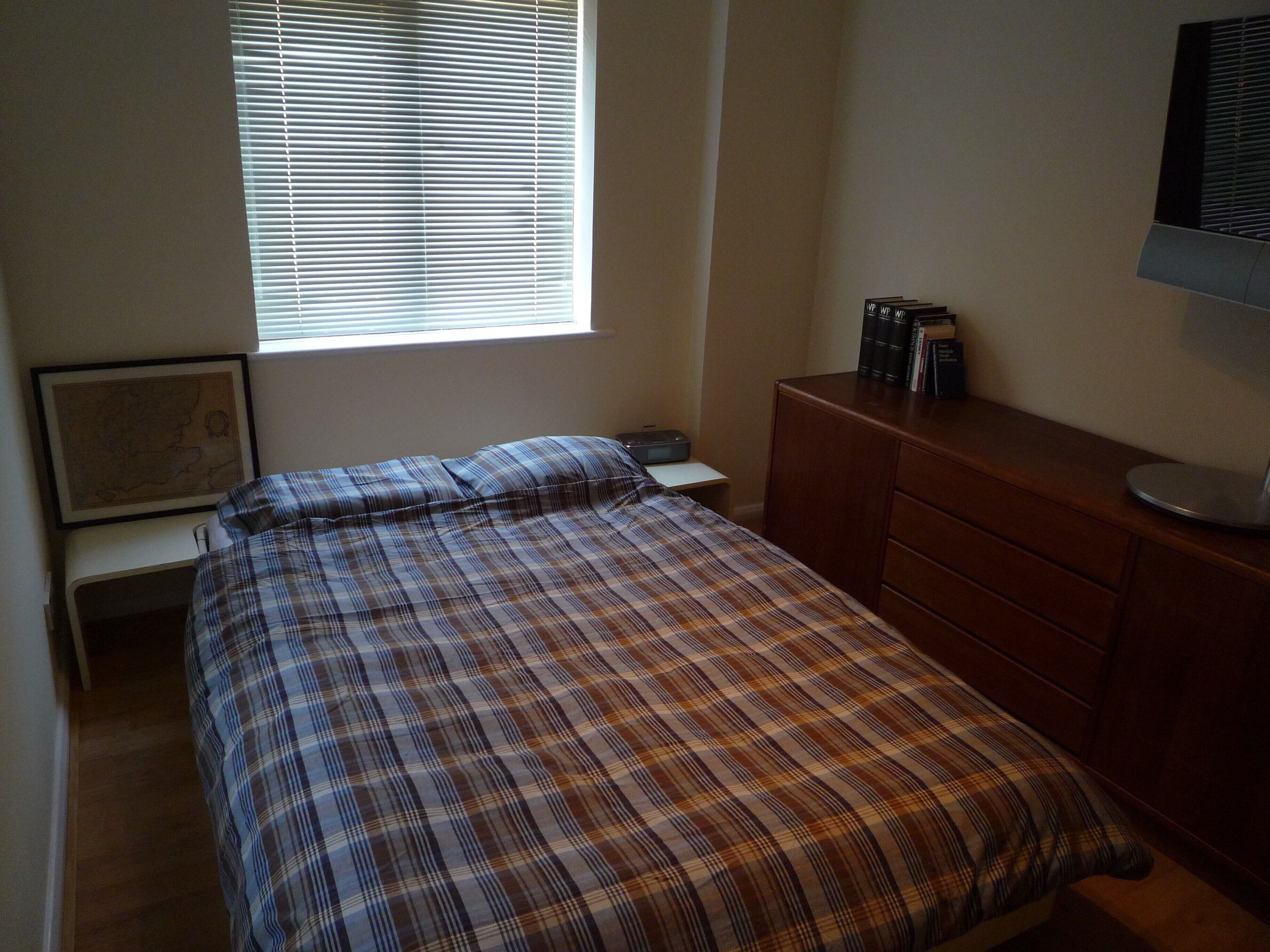 A bedroom with a bed, a dresser, a desk, a map on the wall, and a window with blinds.
