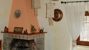 A rustic room with a stone fireplace, wooden beams, a hanging light fixture, and a bed with a patterned bedspread. - Escape from city (Orvieto)