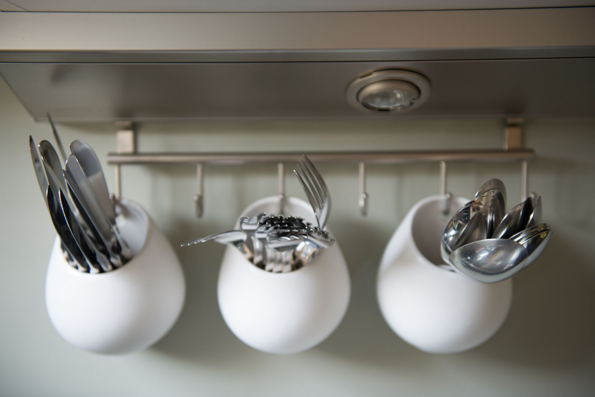 A kitchen with three white mugs hanging on a rack, each containing utensils.
