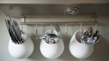 Een keuken met drie witte mokken aan een rek, elk gevuld met bestek.