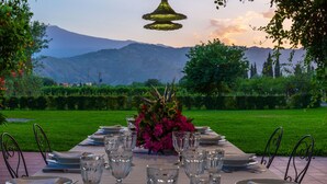 An outdoor dining table set with plates, glasses, and cutlery, with a mountain view in the background.