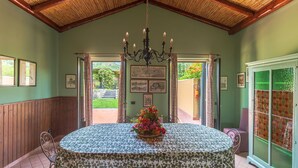 A dining area with a round table, chairs, a chandelier, framed pictures, and a view through open doors.
