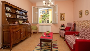 A living room with a wooden cabinet, a red sofa, a table with a red tablecloth, and a window with an open view to the outside. - Villa Mimosa Near Desenzano Old Town Apt 1 Parking, A/C, WiFi, Desenzano Del Garda, Italy (Desenzano Del Garda)