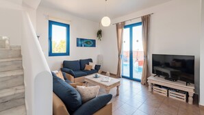 A living room with a sofa, coffee table, TV, and a staircase. - Blue Sea Villa in Gennadi (Gennadi)