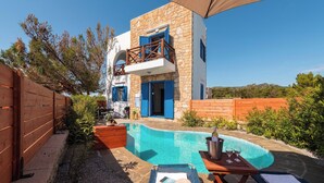 A modern building with a stone facade, a pool, and a wooden deck with lounge chairs. - Blue Sea Villa in Gennadi (Gennadi)