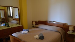 A neatly made bed with a beige bedspread and pillows, a wooden nightstand with a lamp, and a dresser with a mirror.