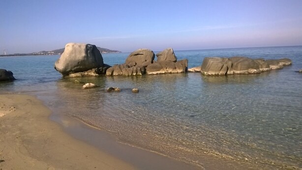 A beach with large rocks in the water and a clear sky.