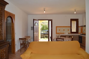 Una habitación con sofá, una mesa de comedor con sillas, una zona de cocina con fregadero y estufa, y una puerta que da al exterior.