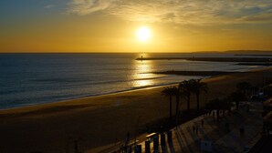 A beach with a sunset, palm trees, and a pier.