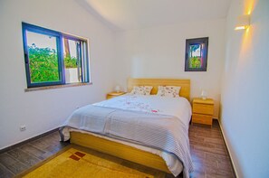 Ein Schlafzimmer mit Bett, Nachttischen, einem Fenster mit Blick und einem Wandbild.
