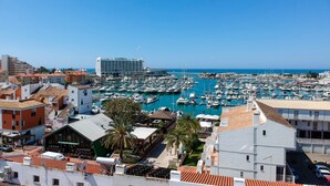 A marina with numerous boats, a large hotel building, and residential buildings with red-tiled roofs.
