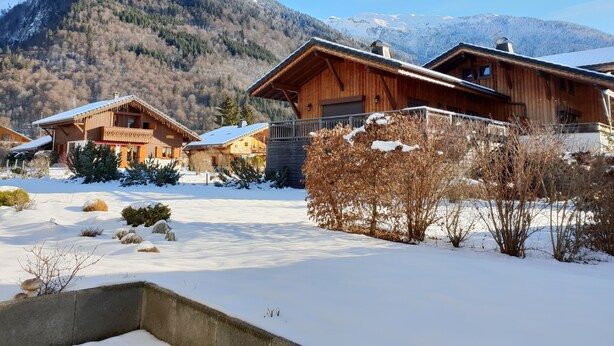 Un chalet en bois doté d’un balcon, entouré d’un paysage enneigé et adossé à des montagnes.