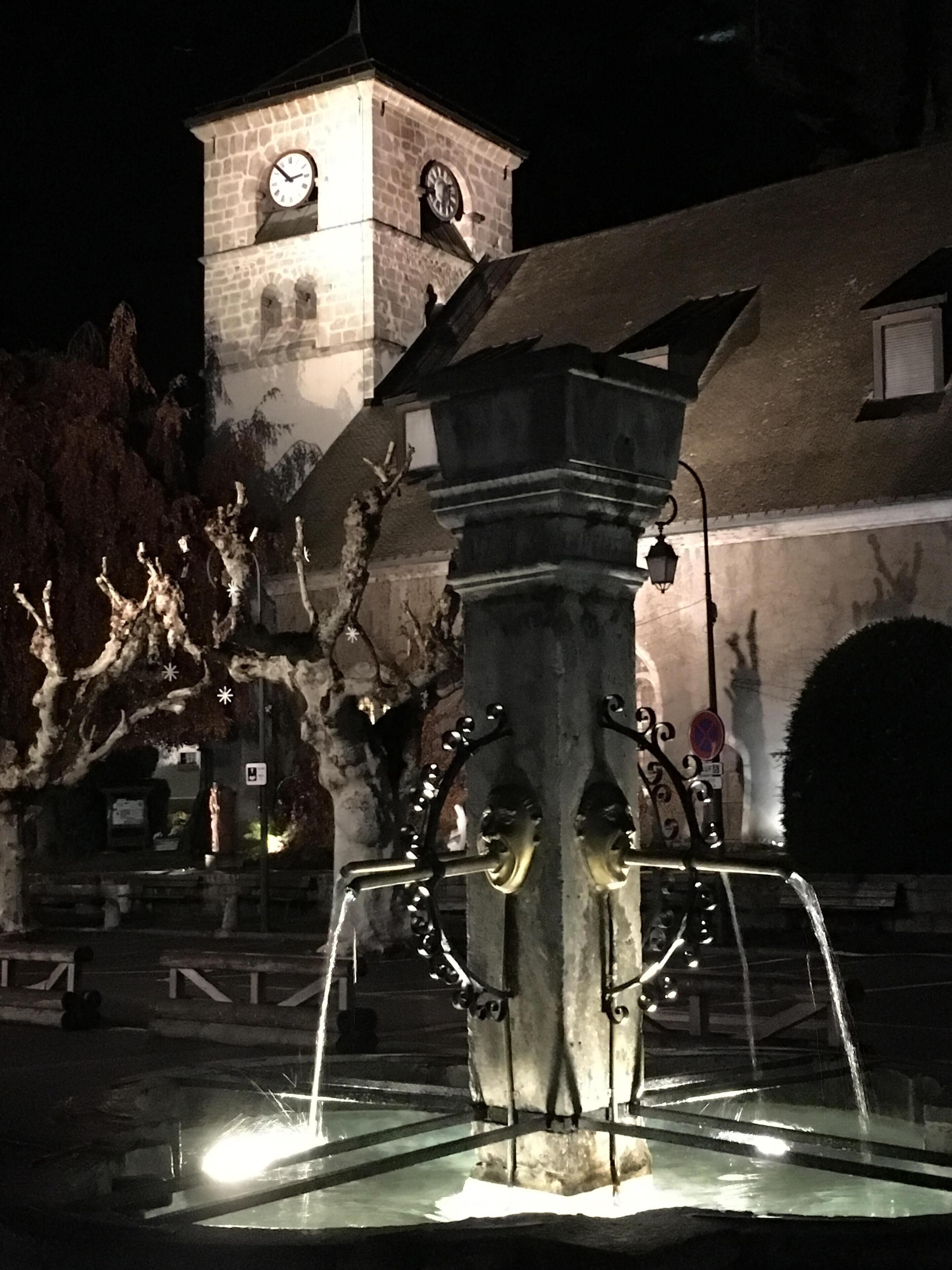 Une fontaine avec un beffroi en arrière-plan.
