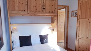 Un lit bien fait, avec du linge de lit blanc et une couverture rouge, une tête de lit en bois, deux lampes de chevet et une armoire en bois.