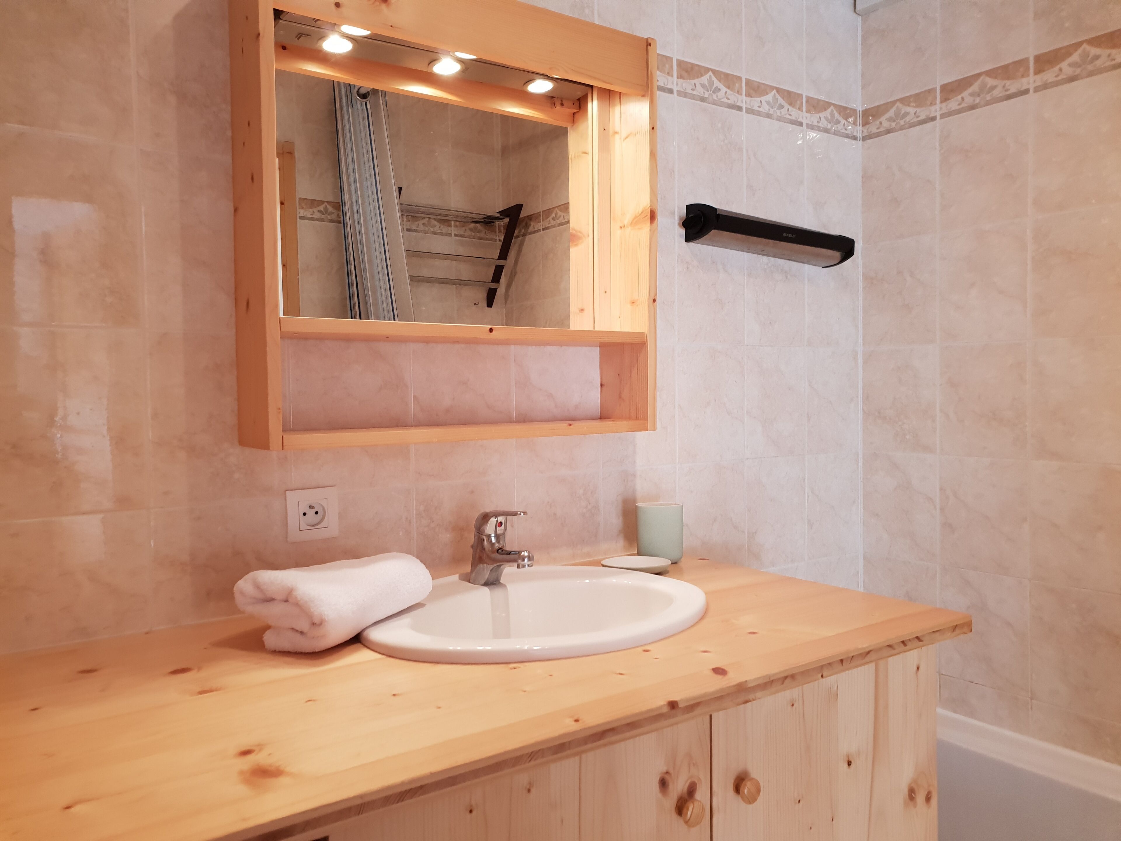 Une salle de bain avec un meuble-lavabo en bois, un lavabo blanc, une serviette et un miroir avec éclairage intégré.
