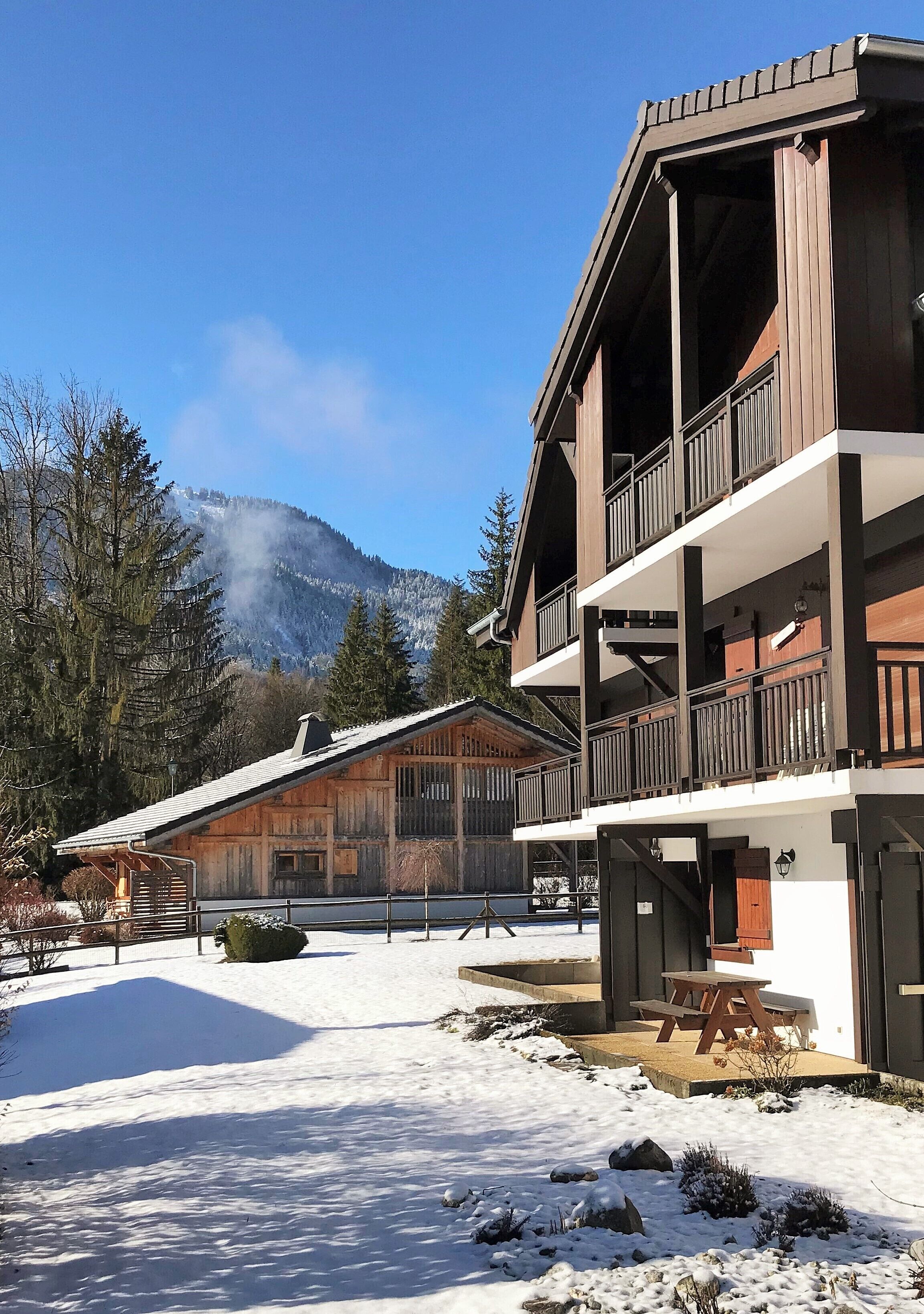 A wooden lodge with a balcony, a covered outdoor seating area, and a view of snow-covered mountains.